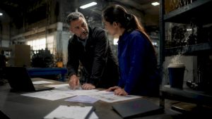 Manufacturing manager and engineer reviewing ERP data on monitor